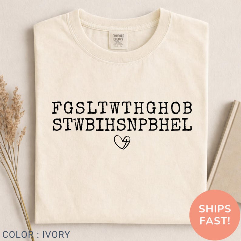 Pu&ograve; includere: T-shirt color avorio con testo nero e simbolo a forma di cuore. Il testo &egrave; in maiuscolo, disposto su due righe. La maglietta &egrave; piegata, con un'etichetta "Comfort Colors". &Egrave; visibile un adesivo rotondo con "Spedizioni veloci!"