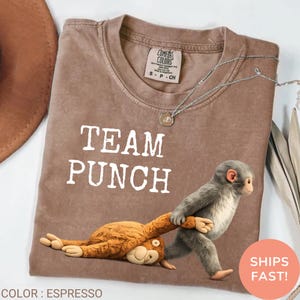 May include: Espresso-colored t-shirt with the text "TEAM PUNCH" in white. A cartoon monkey graphic is featured on the shirt. The shirt is a Comfort Colors brand.