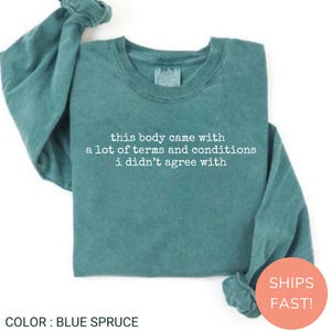 May include: Blue spruce long-sleeved sweatshirt featuring the text "this body came with a lot of terms and conditions i didn't agree with" in white. The sweatshirt has a crew neck and a relaxed fit.