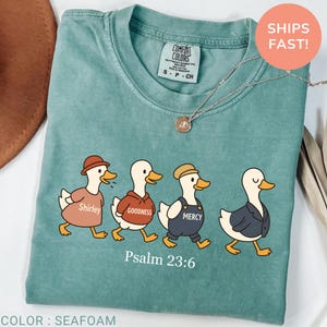 May include: Seafoam green t-shirt featuring a graphic of four ducks in outfits, each labeled with a word: Shirley, Goodness, Mercy. The text "Psalm 23:6" is below the ducks. The shirt has a Comfort Colors tag.