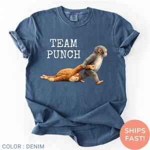 May include: Denim blue t-shirt with the words "TEAM PUNCH" in white. The shirt features a graphic of a gray monkey pulling a brown monkey. The shirt is a crew neck style.