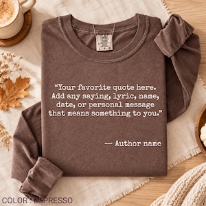 May include: A long-sleeve espresso brown crewneck sweatshirt featuring white text that reads: Your favorite quote here. Add any saying, lyric, name, date, or personal message that means something to you. — Author name. The garment has a Comfort Colors label.
