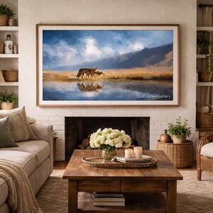 Könnte beinhalten: Gerahmter Landschaftskunst-Druck mit zwei Wölfen an einem Gewässer. Das Kunstwerk zeigt einen blauen Himmel, Berge und warme Farben. Der Rahmen ist hellbraun. Das Bild hängt über einem Kamin.