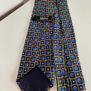 Puede incluir: Una corbata azul marino con un patr&oacute;n repetido de dise&ntilde;os florales azules dentro de cuadrados dorados. La etiqueta dice "Magasin by Florence Style."
