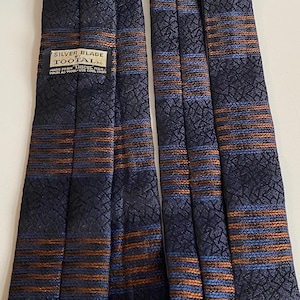May include: Navy blue neckties with a textured pattern and horizontal stripes in shades of orange and blue. The label reads "SILVER BLADE TOOTAL". Made from Tricel. Wash as wool, use cool iron.