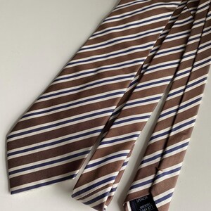 Puede incluir: Una corbata a rayas marrones con rayas blancas y azul marino. La corbata está hecha de una tela suave y está colocada sobre una superficie de color claro. La corbata tiene un diseño clásico, adecuado para vestimenta formal o de negocios.