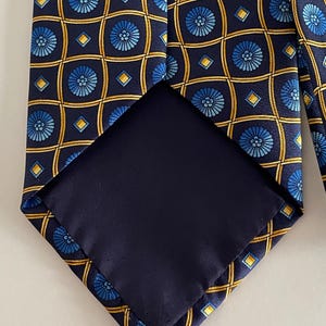 Puede incluir: Una corbata azul marino con un patr&oacute;n repetitivo de dise&ntilde;os florales azules y formas geom&eacute;tricas amarillas. El interior de la corbata es de tela azul marino lisa. Un accesorio cl&aacute;sico.