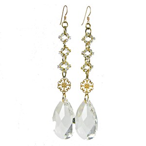 May include: A pair of long, dangling earrings with a gold-tone metal design. The earrings feature clear, faceted teardrop-shaped crystals at the bottom, connected by a chain of gold-tone metal links and clear crystals. The earrings have a hook closure.
