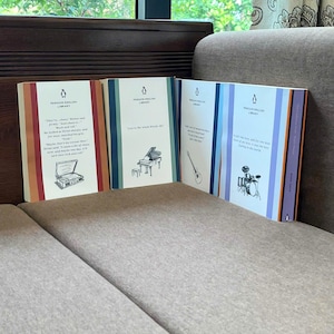 May include: Four Penguin English Library books are displayed, each with a different cover design. The covers feature illustrations of a piano, guitar, and drum set, with quotes. The spines have vertical stripes in various colors.
