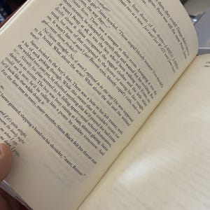 May include: Open book with text on the pages. The text is in black font on off-white paper. The book is open to a page with a paragraph about a boy and his feet. The book is on a dark surface.