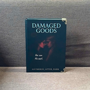 K&ouml;nnte beinhalten: Ein dunkelgr&uuml;nes Hardcover-Buch mit dem Titel "DAMAGED GOODS". Auf dem Cover sind zwei Silhouetten und der Text "Her scar. His mark." zu sehen. Goldene Buchecken sind vorhanden. Der Name des Autors, "SLYTHERIN_AFTER_DARK", steht unten.