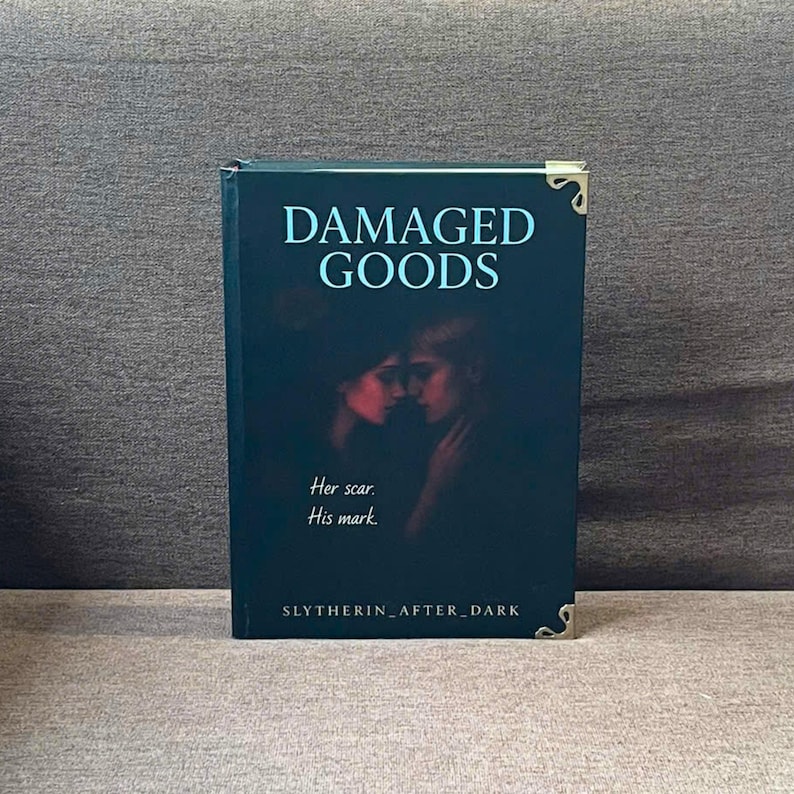 K&ouml;nnte beinhalten: Ein dunkelgr&uuml;nes Hardcover-Buch mit dem Titel "DAMAGED GOODS". Auf dem Cover sind zwei Silhouetten und der Text "Her scar. His mark." zu sehen. Goldene Buchecken sind vorhanden. Der Name des Autors, "SLYTHERIN_AFTER_DARK", steht unten.