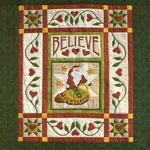 May include: A quilted Christmas wall hanging with a green background. The central panel features Santa Claus and the word "BELIEVE". The quilt is bordered with red, white, green, and yellow geometric and floral patterns. A festive holiday decoration.