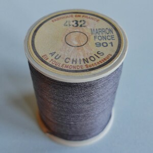 以下が含まれることがあります： 「Fabriqué en France」と「Au Chinois」と書かれたラベルが付いた、濃い茶色の糸の糸巻き。糸は白い糸巻きにしっかりと巻き付けられています。ラベルには「Marron Fonce 901」という文字も含まれています。