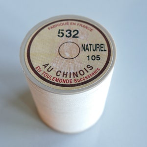 Puede incluir: Una bobina de hilo blanco con una etiqueta marrón que dice "Fabrique en France 532 Naturel 105 Au Chinois Ets Toulmonde Successeurs".