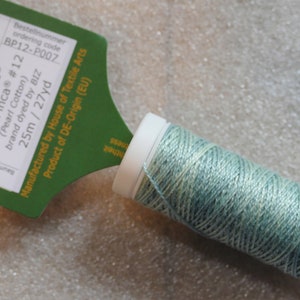 May include: A spool of light blue and green pearl cotton thread, labeled "P007 Agave Presencia® Perlé Finca #12 (Pearl Cotton) brand dyed by BIZ 25m/27yd BP12-P007 ordering code Bestellnummer".