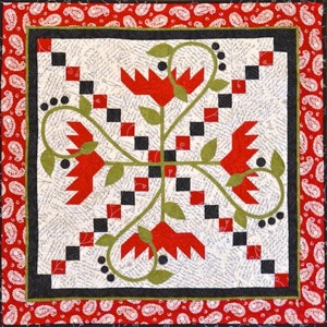 May include: A handmade quilt with a central floral design in red, green, and black on a cream background. The quilt features a red paisley border and a black inner border. The floral design includes red stylized flowers and green leaves.