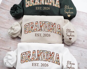 May include: Three sweatshirts in green, beige, and white, each with "GRANDMA" in floral letters and "EST. 2026." Sleeves feature names "Ethan Sophia" and a heart. The sweatshirts are displayed on a light wood surface.