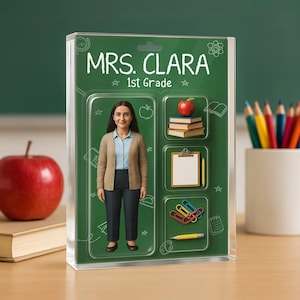 May include: A clear acrylic block featuring a figure of a teacher, Mrs. Clara, with the text "MRS. CLARA 1st Grade". The background is green with school-themed icons. A red apple and pencils are in the background.