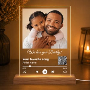 May include: A personalized LED night light featuring a photo of a father and child, with the text "We love you Daddy!" and a music player interface design. The light sits on a wooden base and emits a warm glow.