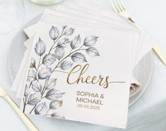 May include: White napkins with a gold foil design of leaves and the text "Cheers Sophia & Michael 05.05.2025".