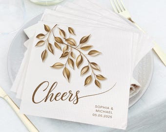 May include: White paper napkins with a gold leaf design and the text "Cheers" printed on them. The napkins also include the text "Sophia & Michael 05.05.2025".