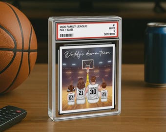 May include: A framed print with the text "Daddy's dream team" featuring a family of four in basketball jerseys. The frame is encased in a clear protective case, with a basketball and a can in the background.