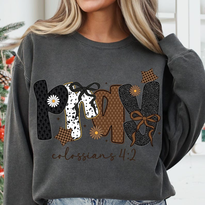 May include: Dark gray sweatshirt with the word "PRAY" in a decorative font. The letters are black, white, and brown with floral and bow accents. The text "colossians 4:2" is printed below the word "PRAY".