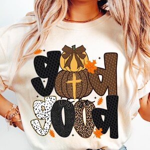 May include: Cream-colored sweatshirt with the phrase "God is so Good" in a mix of patterned fonts. The design includes a pumpkin with a cross and fall leaves, perfect for autumn.