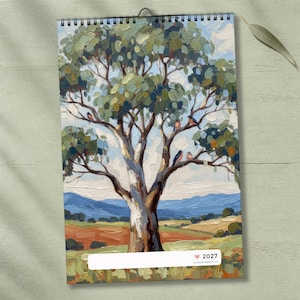 May include: A 2027 wall calendar featuring an oil painting of a large eucalyptus tree with textured green leaves and brown branches. Several small birds are perched on the limbs. The background shows rolling hills, fields, and a blue sky.