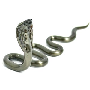 May include: A silver-colored cobra snake figurine with a raised hood. The snake is coiled in a classic pose with its head held high.