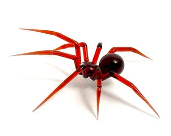 May include: A red glass spider sculpture with eight legs and a round body. The spider is posed in a crawling position with its legs extended.