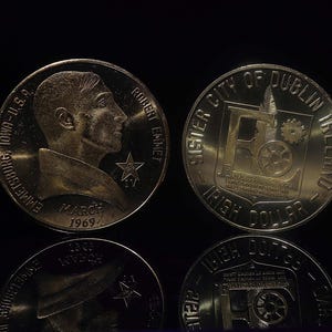 May include: Two silver coins. One coin features a profile of Robert Emmet, the text "EMMETSBURG, IOWA-U.S.A.", "MARCH 1969", and "ROBERT EMMET". The other coin reads "SISTER CITY OF DUBLIN IRELAND" and "IRISH DOLLAR".
