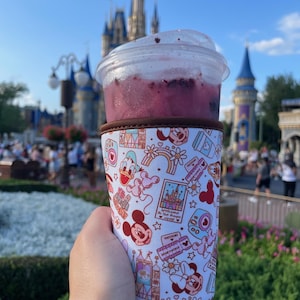 May include: A white insulated cup sleeve with a pink and red Mickey Mouse and Minnie Mouse design. The sleeve features various Disney park icons and the text "Welcome to the Most Magical Place on Earth".