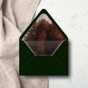 May include: A dark green envelope with a landscape painting visible inside. The painting features a forest scene with trees in shades of brown and red. The envelope is open, revealing the artwork within.