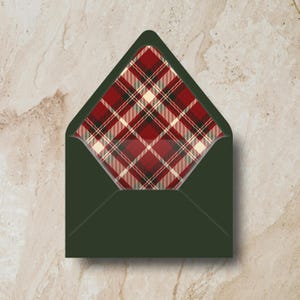 May include: A dark green envelope with a plaid interior. The plaid pattern features red, cream, and black lines. The envelope is open, revealing the patterned interior. The background is a light beige marble.