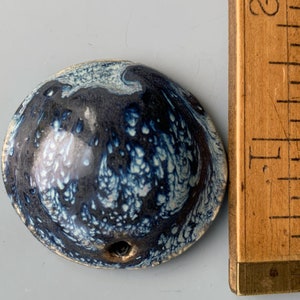 May include: A small, round, ceramic bowl with a blue and white marbled glaze. The bowl has a small hole in the bottom.
