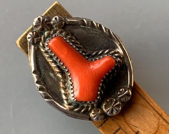 May include: A silver ring with a red coral stone set in a silver bezel. The ring is decorated with a rope design and silver accents.