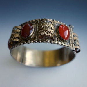 May include: A silver bracelet with intricate filigree work and three red carnelian stones.
