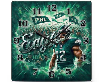 May include: A square wall clock featuring a football player in a teal jersey with the number 12, surrounded by a cheering crowd, green flags with the text PHI, and the word Eagles in script. The clock face has black numbers and black hands.