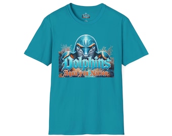 May include: A teal short-sleeve t-shirt featuring a graphic of a dolphin head centred above the text "Dolphins" in blue and "Aqua Fin Nation" in orange. The design includes coral reef elements and is set against a dark, textured background.