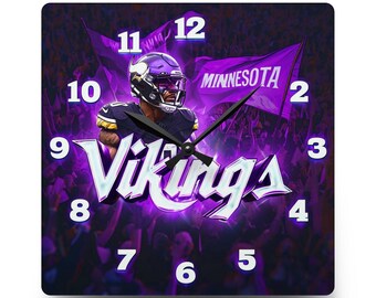 May include: A square wall clock featuring a Minnesota Vikings football player in a purple and gold uniform, a purple flag with the text MINNESOTA, and the word Vikings in large white letters. The clock face has white numbers from 1 to 12.