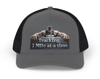 May include: A grey and black trucker cap featuring a graphic of a muscular figure wearing a black tank top with the text Tar Top, holding a sign that reads Trucking, 1 Mile at a time in silver metallic lettering against a dark grey background.