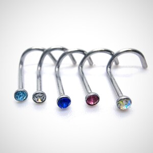 Peut inclure: Cinq anneaux de nez argentés avec des pierres précieuses de différentes couleurs. Les pierres sont bleues, claires, bleu foncé, roses et irisées.