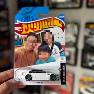 May include: A white BMW M3 toy car in a clear plastic blister pack on a custom card. The card features a photo of three people, the text Happy Father's Day, 2026, 1/1, Fathers Day Edition, and BEST DAD EVER! The car has teal wheels and a black roof.