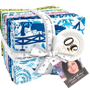 May include: A stack of fabric squares in a variety of blue, green, and pink patterns, tied together with a white ribbon and a measuring tape. The fabric squares feature a variety of designs, including flowers, birds, and geometric patterns. The fabric squares are labeled with the text "Moda Fabrics - Supplies".