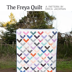 Puede incluir: Patrón de colcha Freya de Erica Jackman. Una colcha colorida con un patrón de chevron en tonos de rosa, azul, verde y gris. La colcha se exhibe al aire libre en un césped.