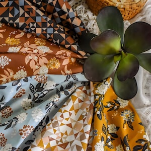 Puede incluir: Una variedad de telas estampadas en varios colores. Las telas presentan diseños geométricos y florales en tonos marrón, azul, amarillo y blanco. También se ven una planta suculenta y una cesta de mimbre.
