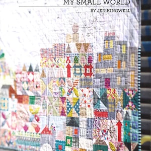 May include: A colorful patchwork quilt with a title that reads "My Small World" by Jen Kingwell. The quilt features a variety of geometric shapes and patterns, including houses, arrows, and stars. The quilt is made with a variety of fabrics in bright colors, including red, yellow, blue, green, and pink.