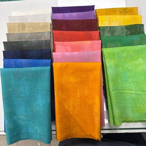 May include: A collection of folded fabric squares arranged in three vertical columns. The fabric features a mottled, textured appearance in a wide spectrum of colors including white, gray, black, blue, teal, purple, red, pink, orange, yellow, and green.